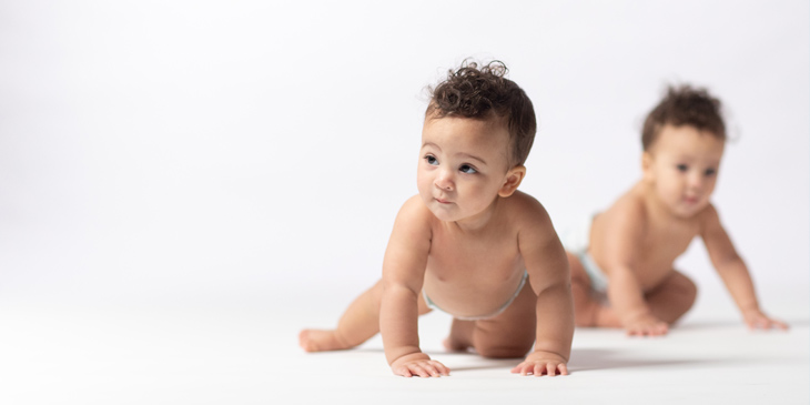 Two Baby Sisters Crawling on a White Seamless, With One Being in Focus and the Other Out of Focus