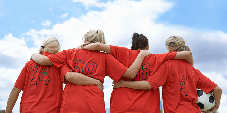 Four women with their arms around each other with one holding a football