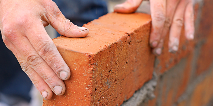 two hands laying a brick in place