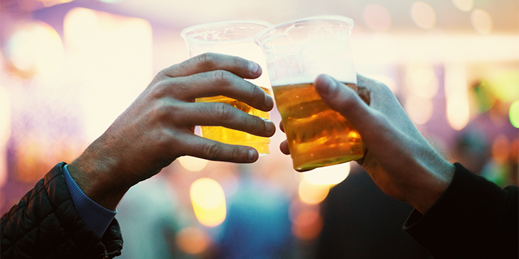 Two half full plastic beer glasses being held together