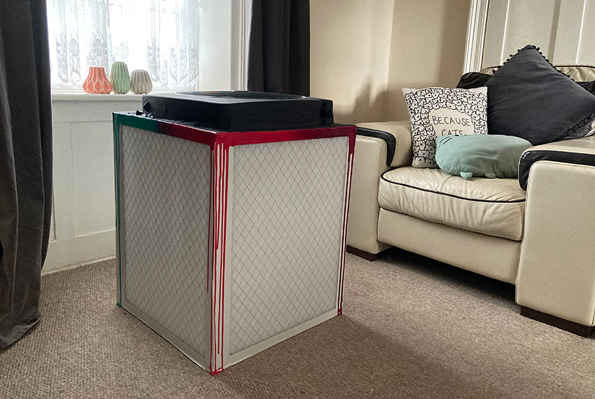 The Corsi-Rosenthal box in complete view in a living room, with a cream chair in the background