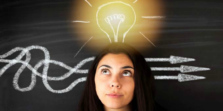 A woman standing in-front of a blackboard, with chalk arrows behind her and a chalk lightbulb above her head