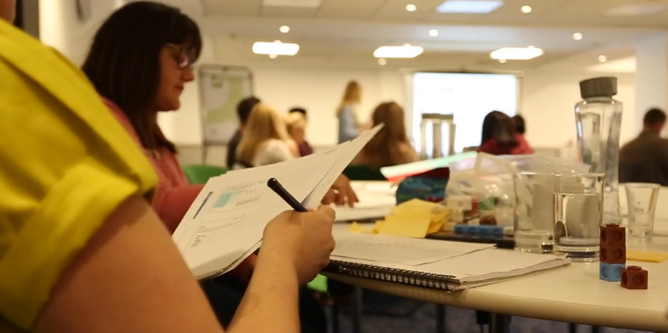 A person holding some papers and pen, in an adult classroom setting