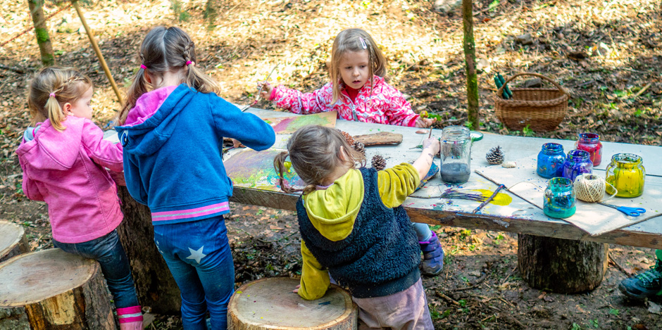 Kindergarten kids having fun drawing and creating on a wooden table in nature