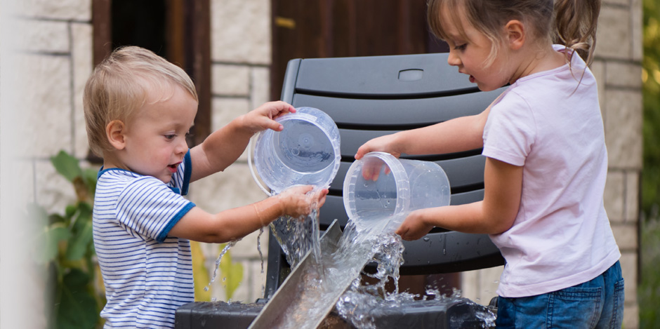 Two children pouring water down a sloping piece of guttering