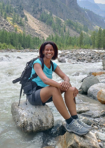 Dr Flavia H. Santos sat on a large stone on a river