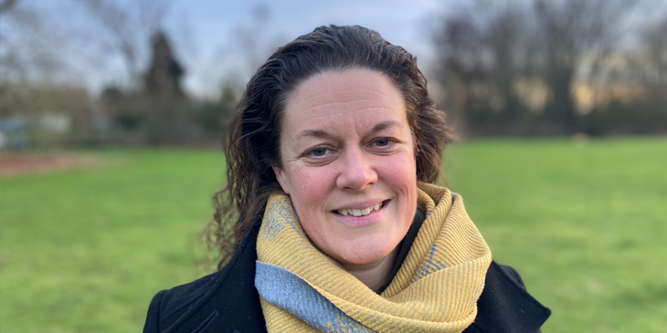 A headshot of Fran in a green field, with trees in the background