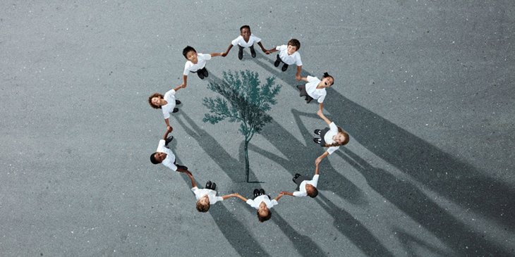 Group of children photographed from above on a tarmac surface with a tree painted on the ground inbetween them