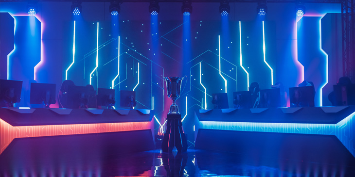 An eSports arena with a winner trophy in the middle, either side there is 5 seats with a monitor each