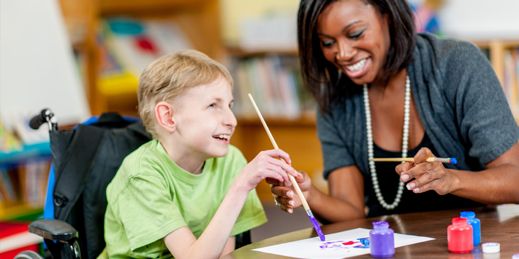 An adult helping a child with learning difficulties to paint