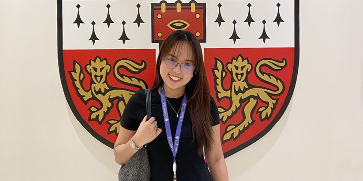 Jireh standing infront of the University of Cambridge badge