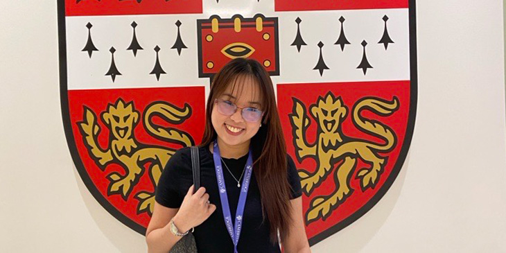 Jireh standing infront of the University of Cambridge badge