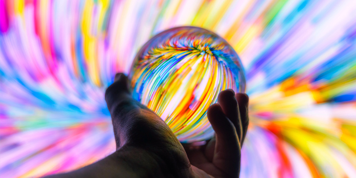 A hand holding a crystal ball, which is reflecting a swirling pattern of colours in the background