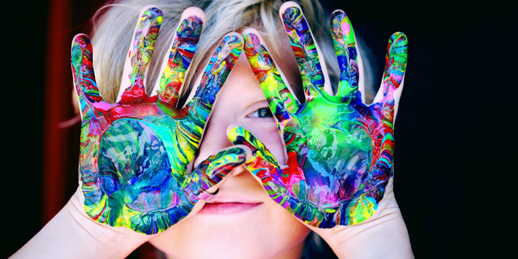 A child's hands covered in paint raised in-front of her hands