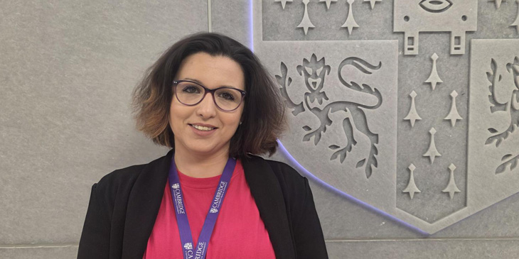 Headshot of Nadezhda standing infront of a wall with 1/4 of the University of Cambridge crest shown