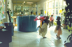 Three children in a bright corridor filled with plants and plinths