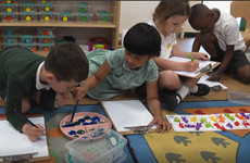 Four children working on maths problems in pairs, using different sets of manipulatives