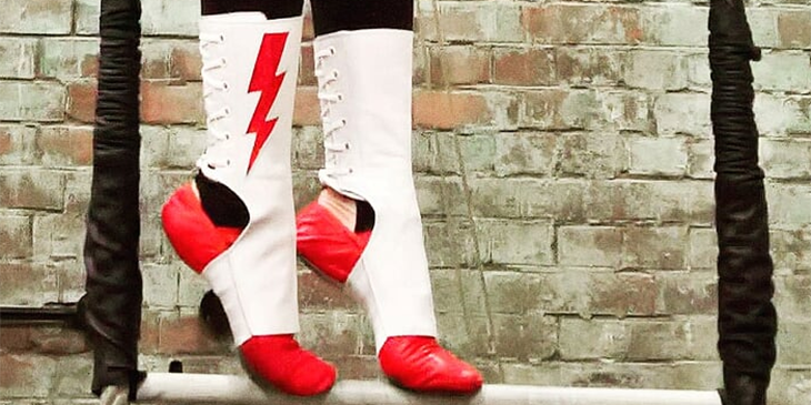 A pair of feet on tiptoe wearing red and white trapeze shoes